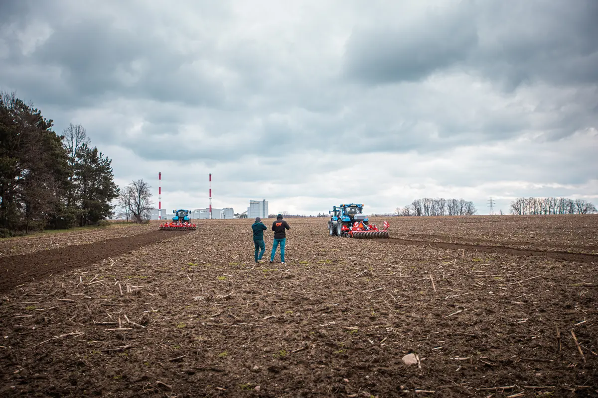Prace na polu Ciągniki uprawiają pole, a dwaj obserwatorzy stoją na środku gruntu podczas prac polowych.