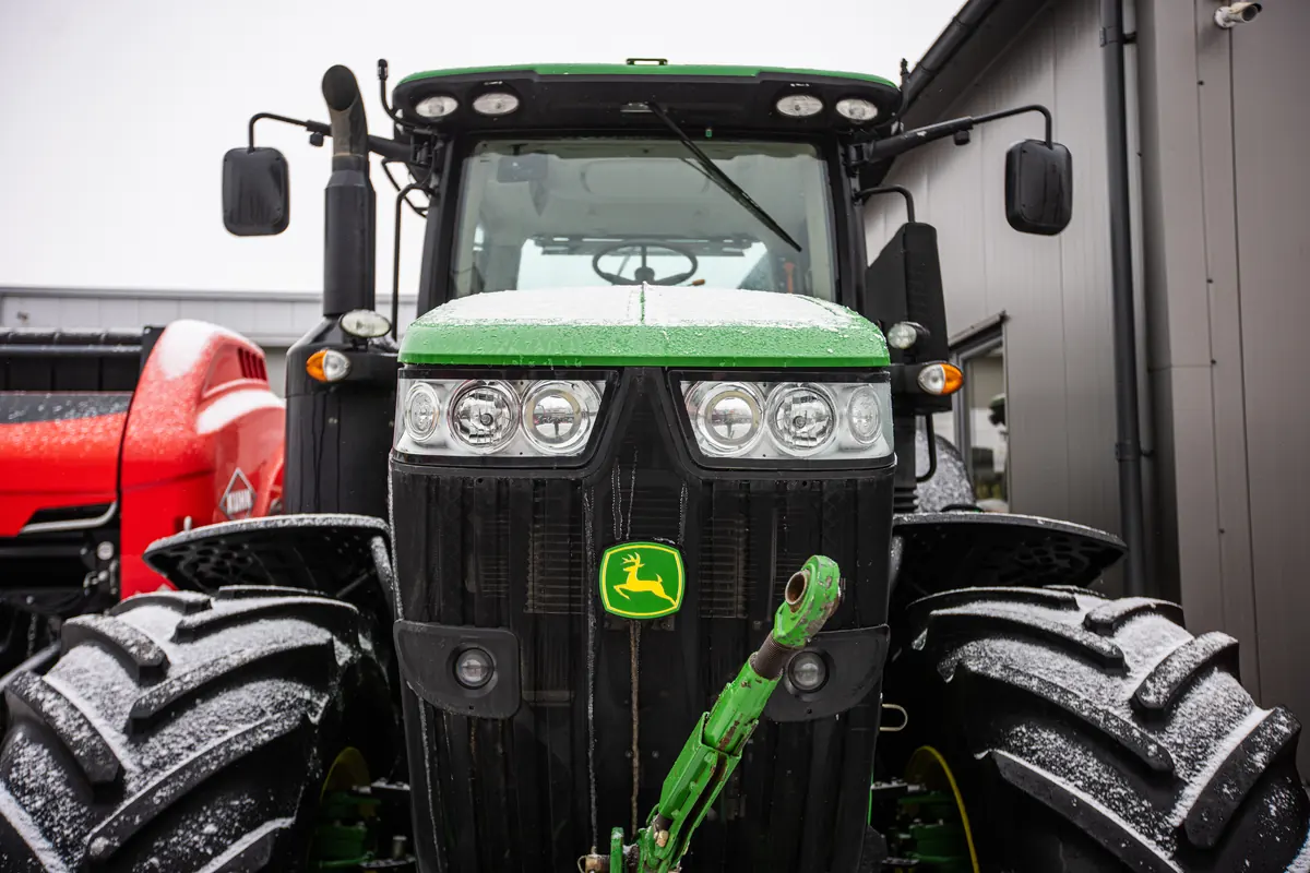 Ciągnik przed zimowym przeglądem Zielony ciągnik John Deere z oszronionymi oponami stoi przed budynkiem gospodarczym.